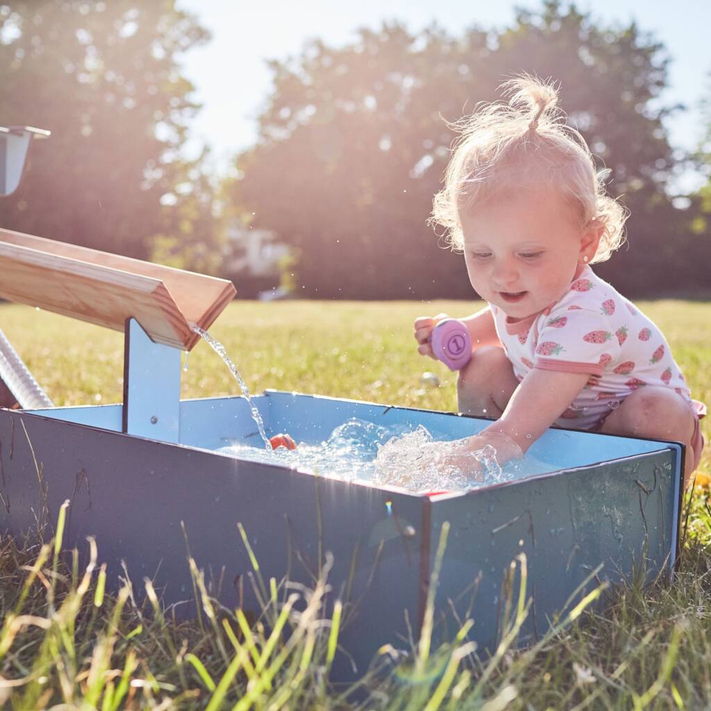 Kind spielt mit Wasserrinne am Wasserspielgerät im Außengelände.